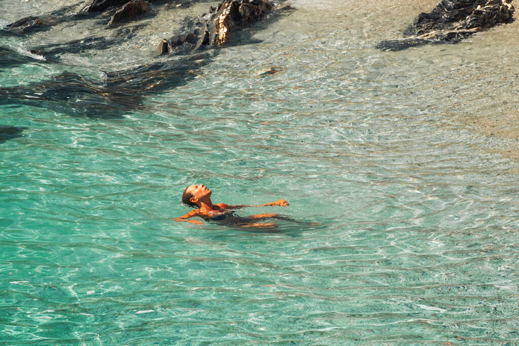 Person floating in clear turquoise water near a rocky shoreline Copy alt text